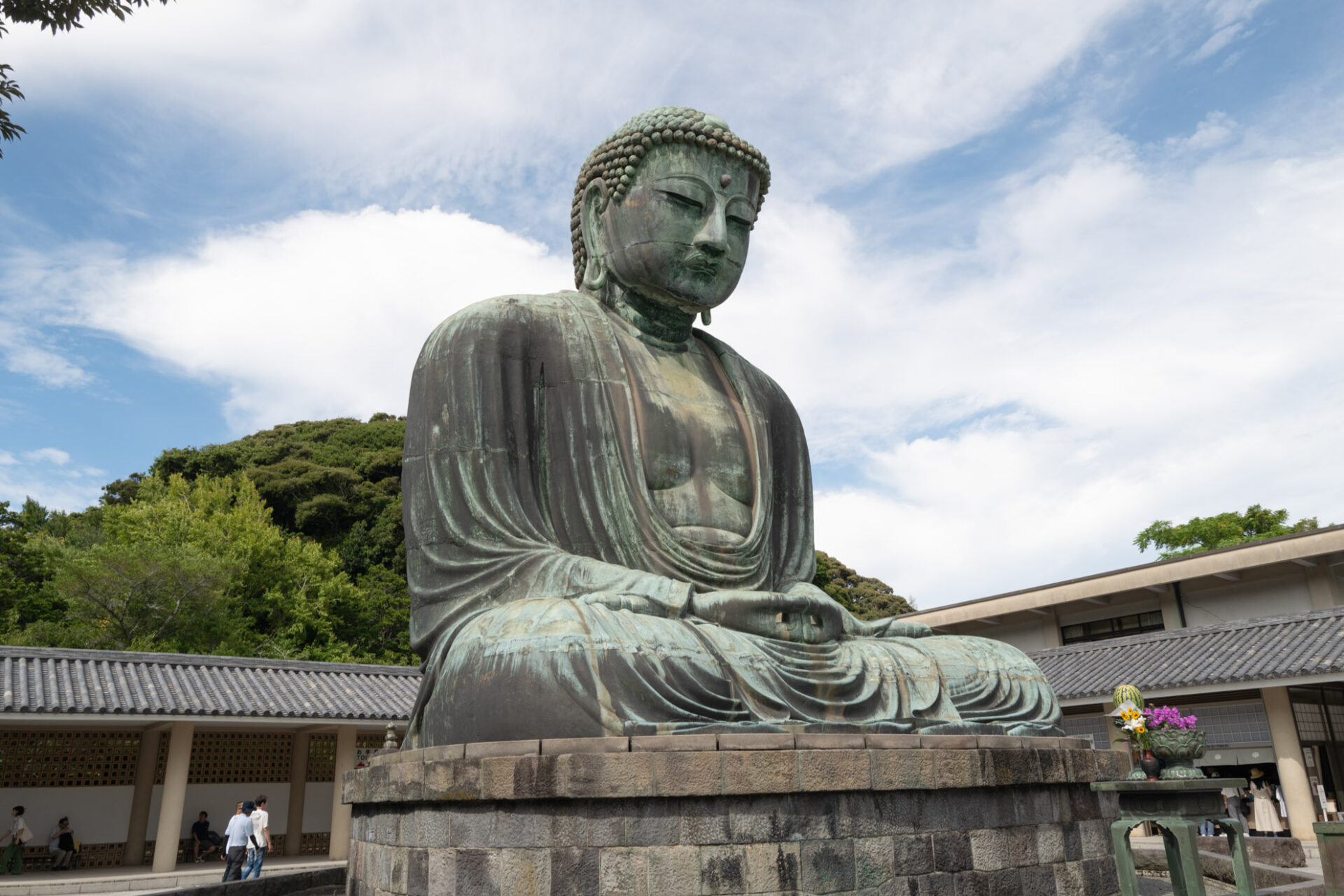 Statua del Grande Buddha di bronzo a Kamakura, Giappone, con cielo nuvoloso in sfondo e alberi verdi.